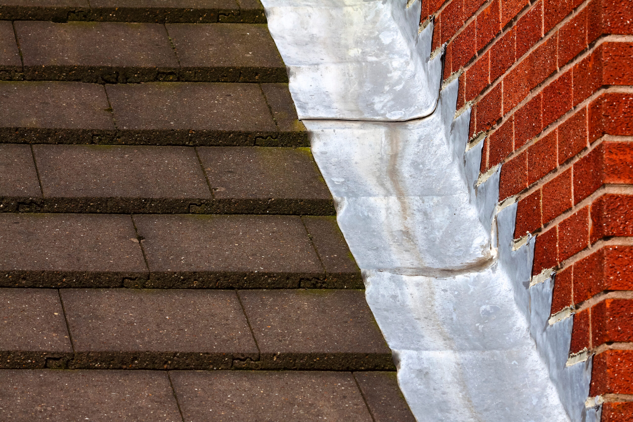 Stepped lead flashing roof gulley creating a water tight seal between roof tiles and brick wall on a domestic house.